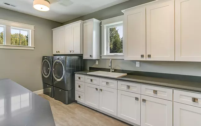 White Shaker laundry cabinets run with large sink.